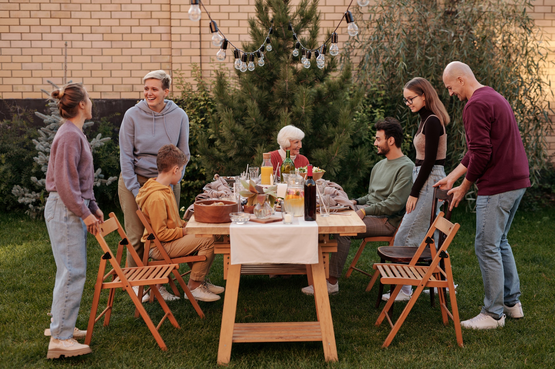 Family get together around an outdoor table with food and wine. Lots of people smiling and socialising